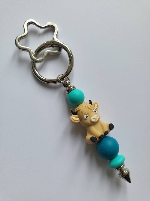 Tashanger met koetje in blauw, beige en turquoise.