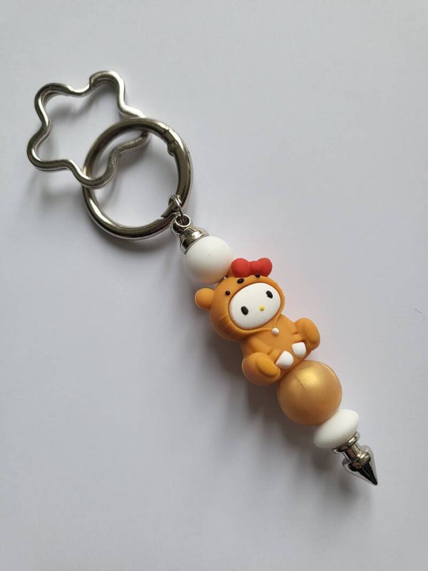 Tashanger met baby-figuurtje in goud, beige en wit.