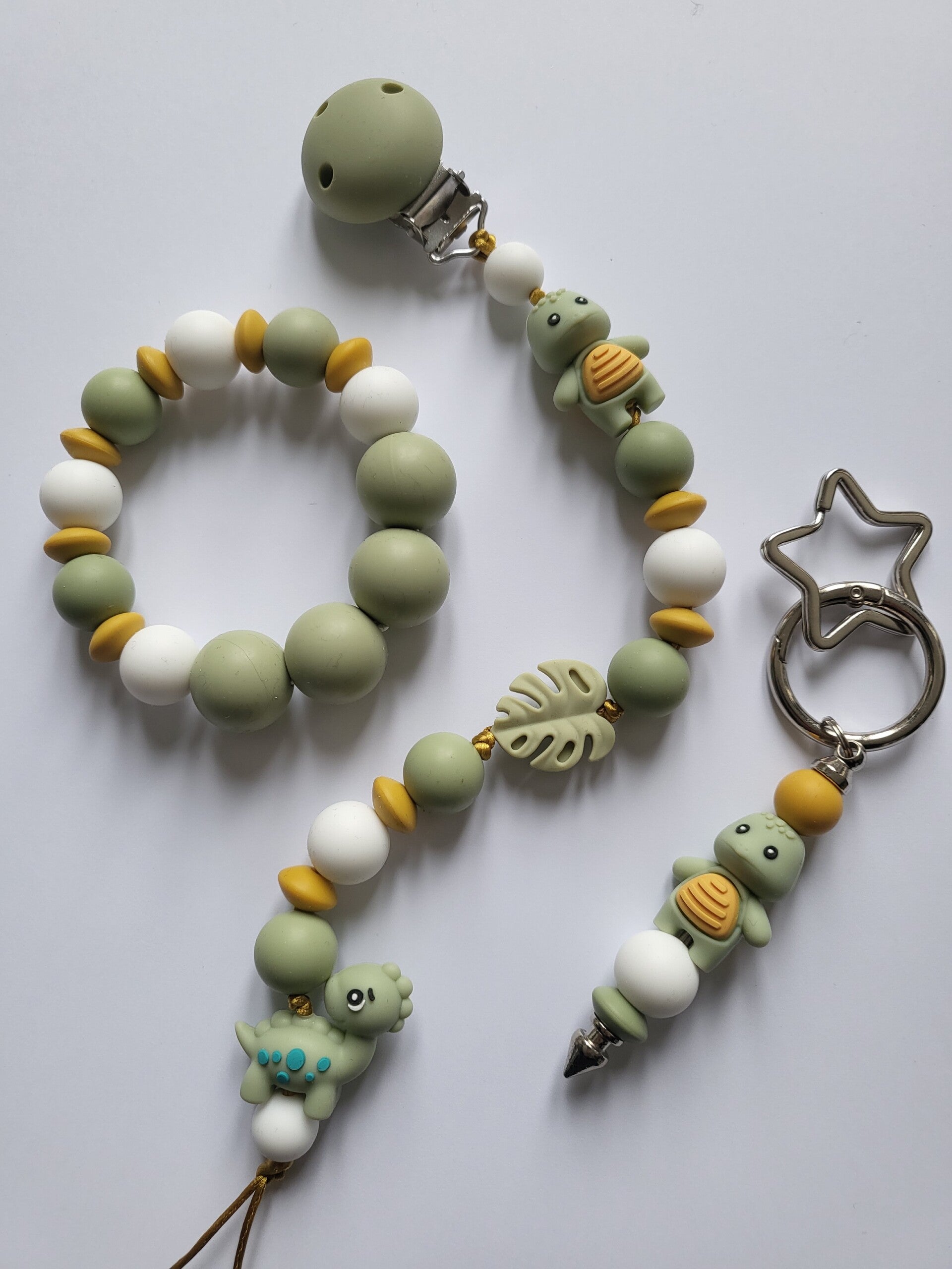 Speenkoord en bijtring met schildpadje en dinosaurusje in matcha-groen, okergeel en wit.
