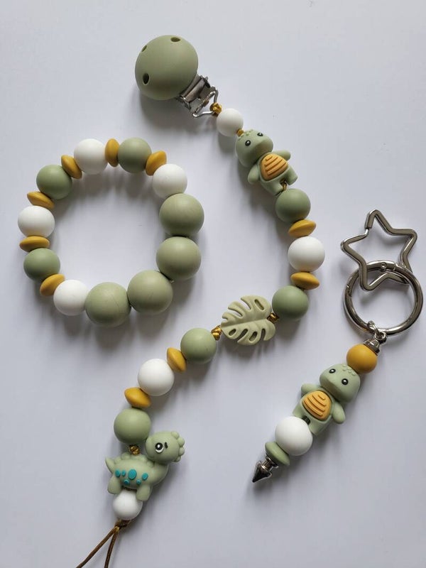 Speenkoord en bijtring met schildpadje en dinosaurusje in matcha-groen, okergeel en wit.