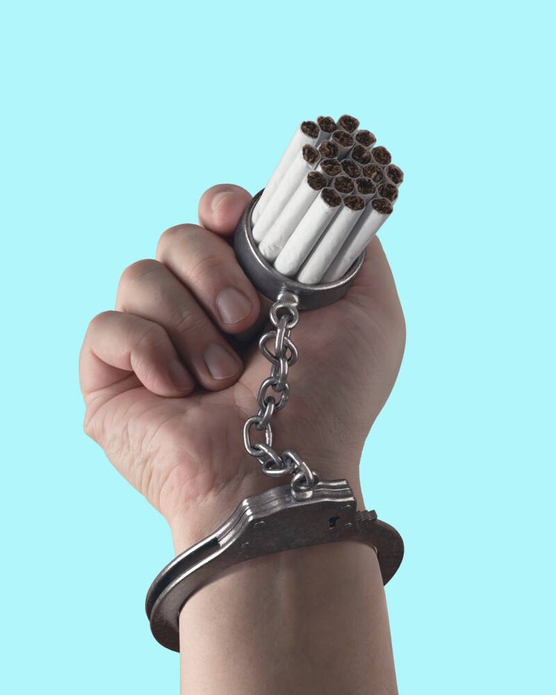 mano sosteniendo una cadena con cigarrillos, simbolizando la adicción y la necesidad de liberación.