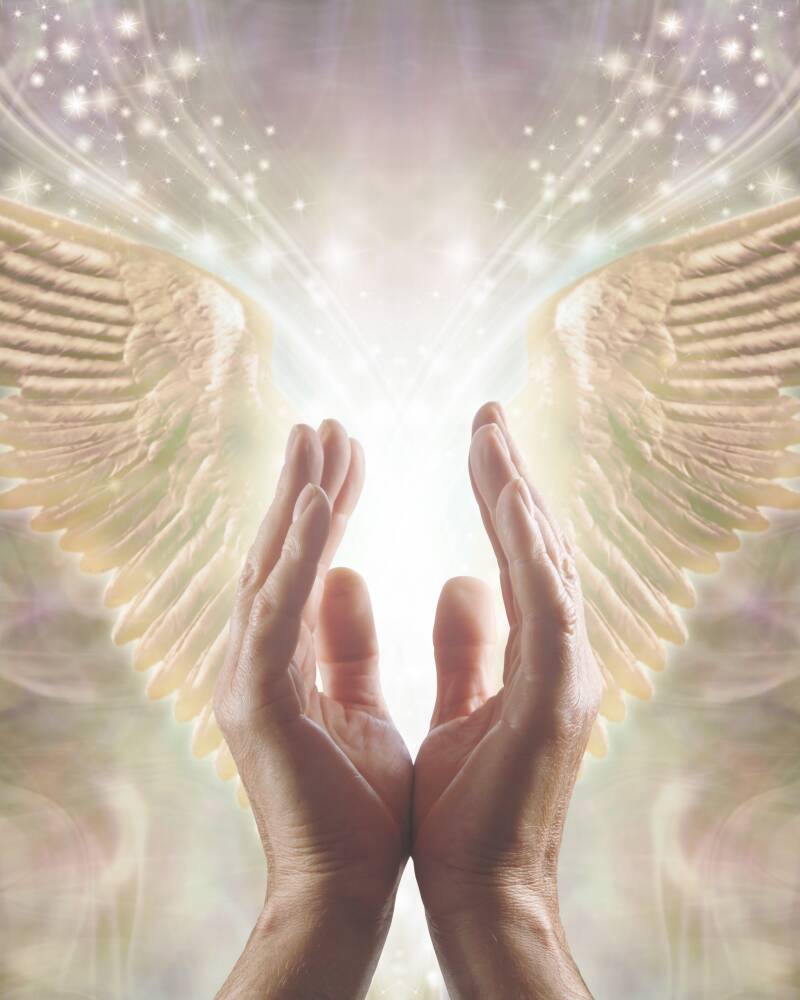 manos elevadas hacia unas alas doradas de ángel con luz brillante, símbolo de sanación espiritual y conexión con energías celestiales