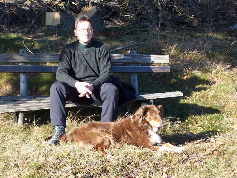 Der Hundezüchter von Magic Dream of  Black Forest sitzt auf einer Bank am Waldrand, davor liegt sein Ersthund