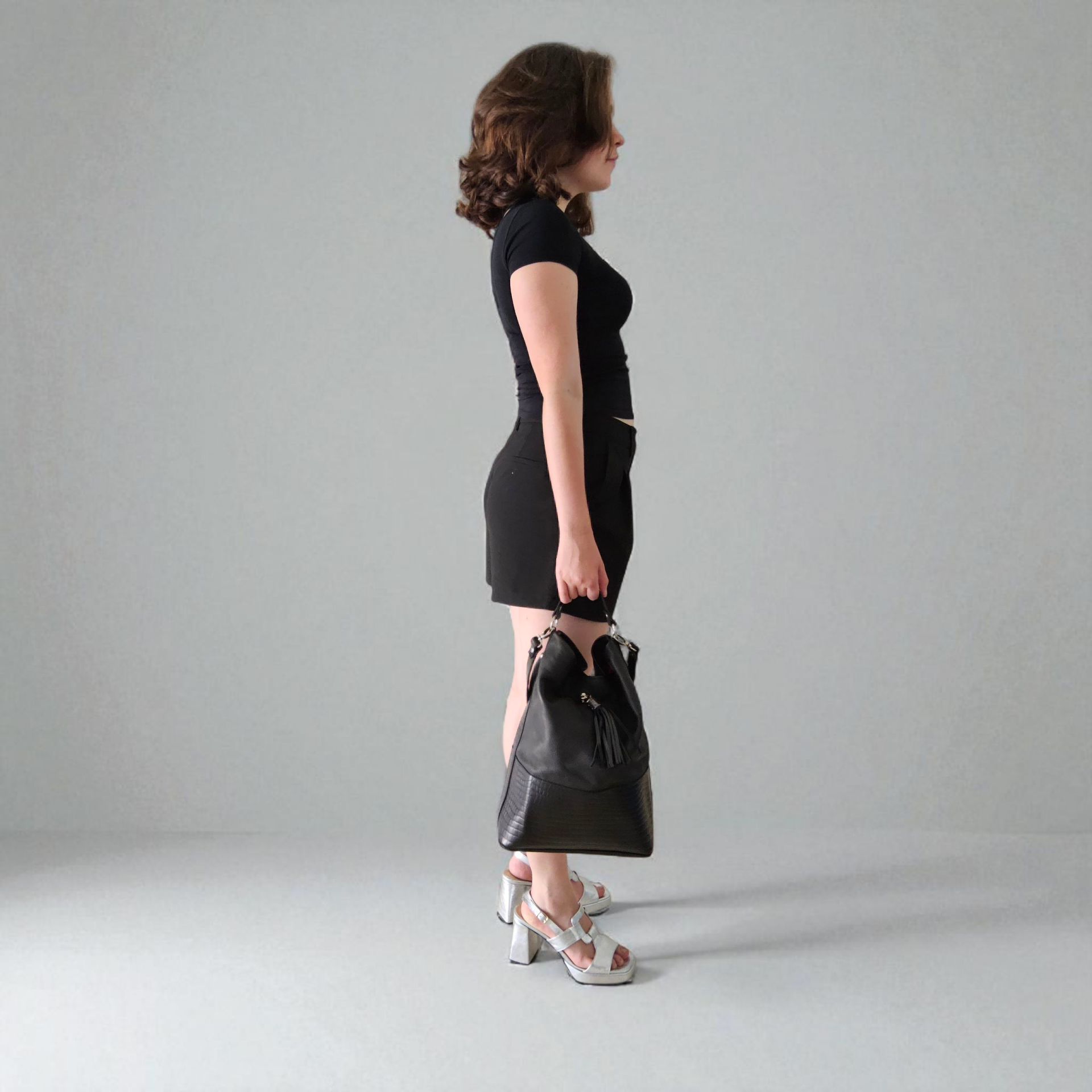 Frau schwarz gekleidet mit Silbersandaletten, Shopper aus schwarzem Leder, Reptilienprägung und Quaste