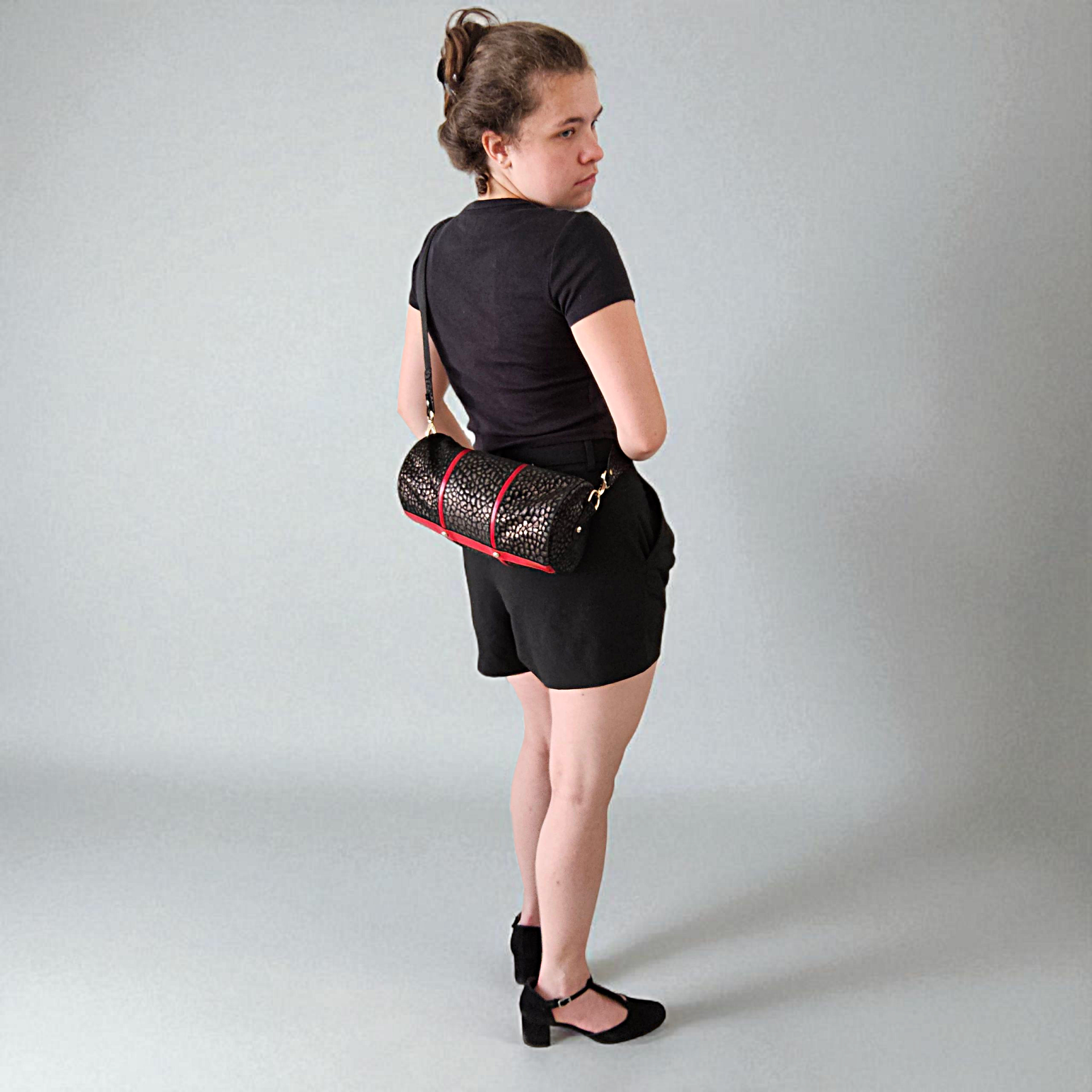 Frau mit Ledertasche in Zylinderform, Reptilienprägung mit roten Streifen