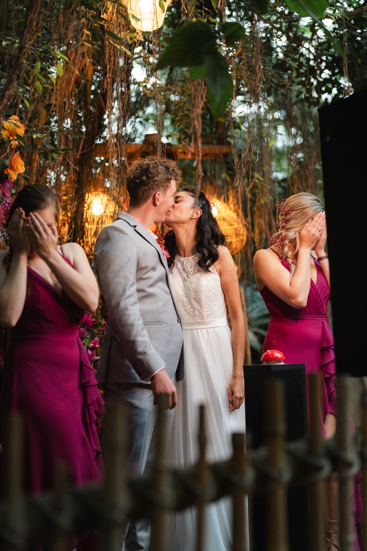 Bruidspaar staat voor de photobooth en kust elkaar. De twee bruidsmeisjes slaan hun handen voor hun ogen voor de grap. Achtergrond is tropisch; Jungle Dome in Center Parcs Heijderbos. Weddingplanner Elvira Patelias, Wedding and Dreams. Foto: Leafsum.