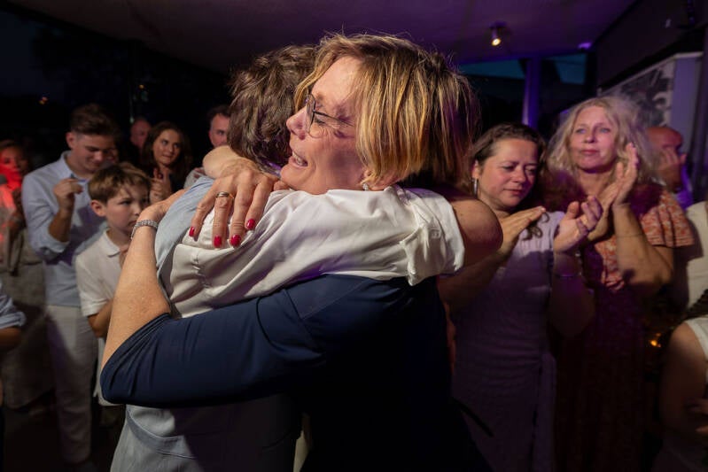 Liefdevol moment wenshuwelijk. De bruidegom omhelst weddingplanner Elvira Patelias.