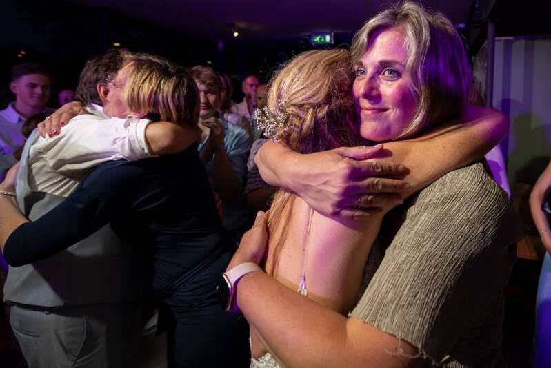 Het bruidspaar van het wenshuwelijk geeft weddingplanners, Elvira Patelias en Corrie Weijers, een knuffel als dank voor de organisatie van hun bruiloft. 