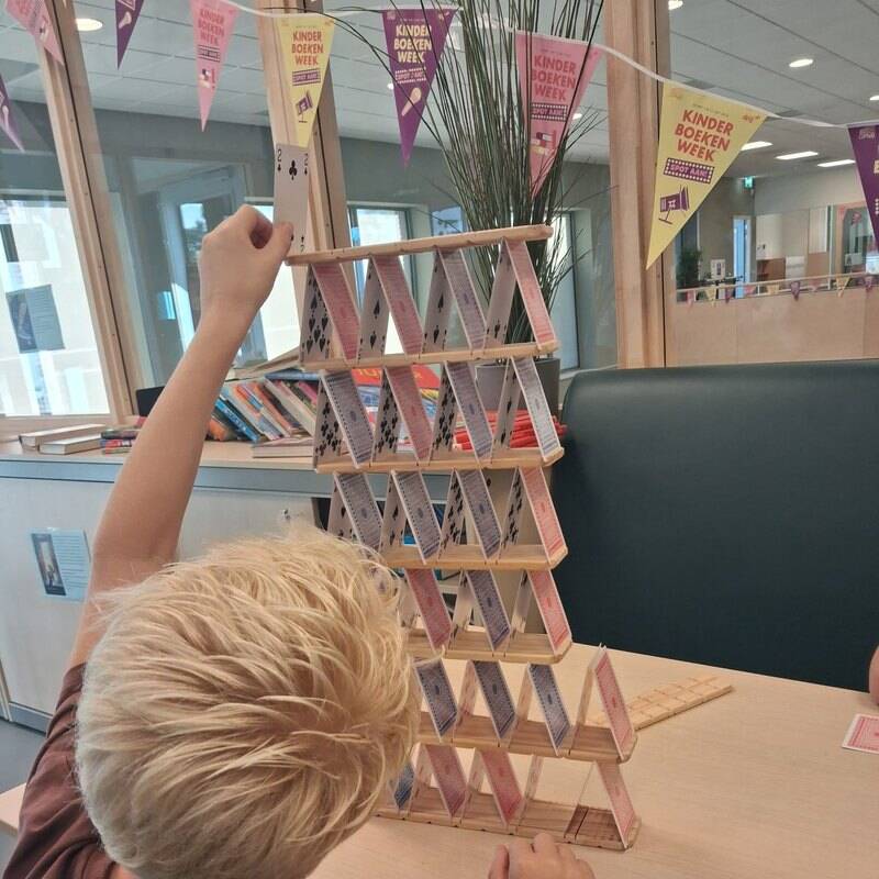 Een jongen zet de bovenste verdieping op een kaartenhuis van CABU-plankjes