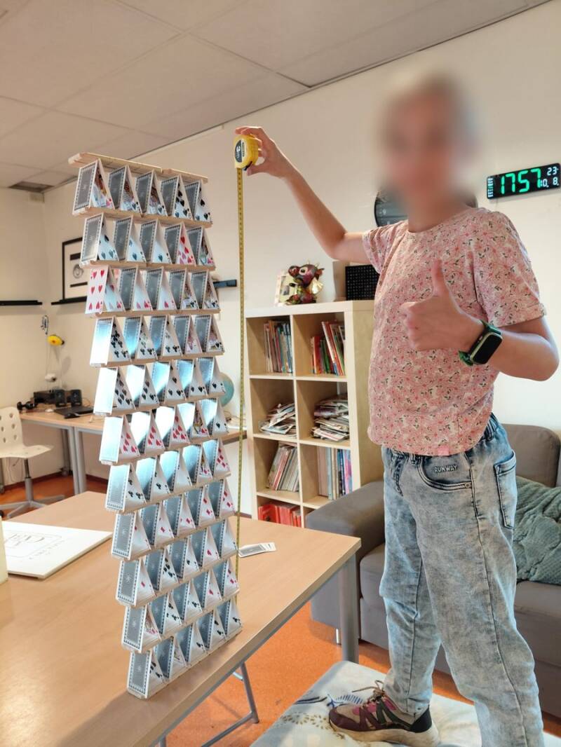 Een meisje staat naast een kaartenhuis van CABU-plankjes dat hoger is dan zijzelf