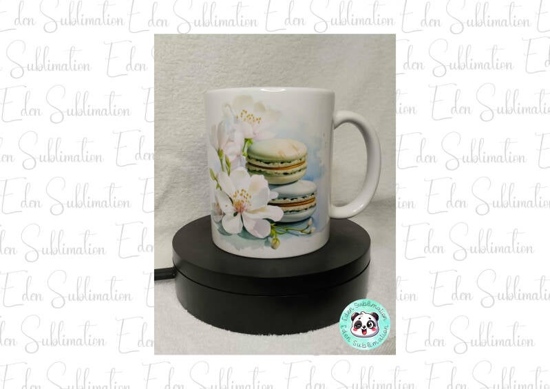 Mug blanc décoré de macarons pastel empilés et de fleurs blanches délicates sur fond clair.