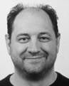 A black and white headshot of the author Frank De Witte smiling  with a beard and thinning hair.