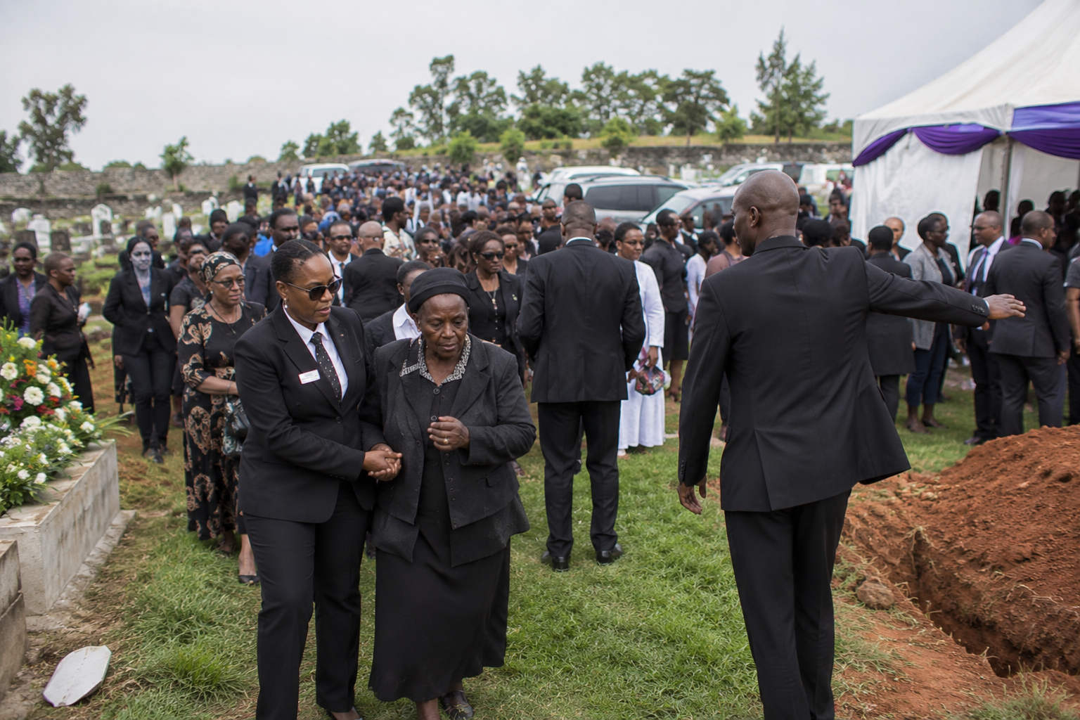 Professional funeral ushers coordinating crowd movement and assisting family members during a burial ceremony, guiding mourners and organizing graveside gatherings at a cemetery in Kenya.
