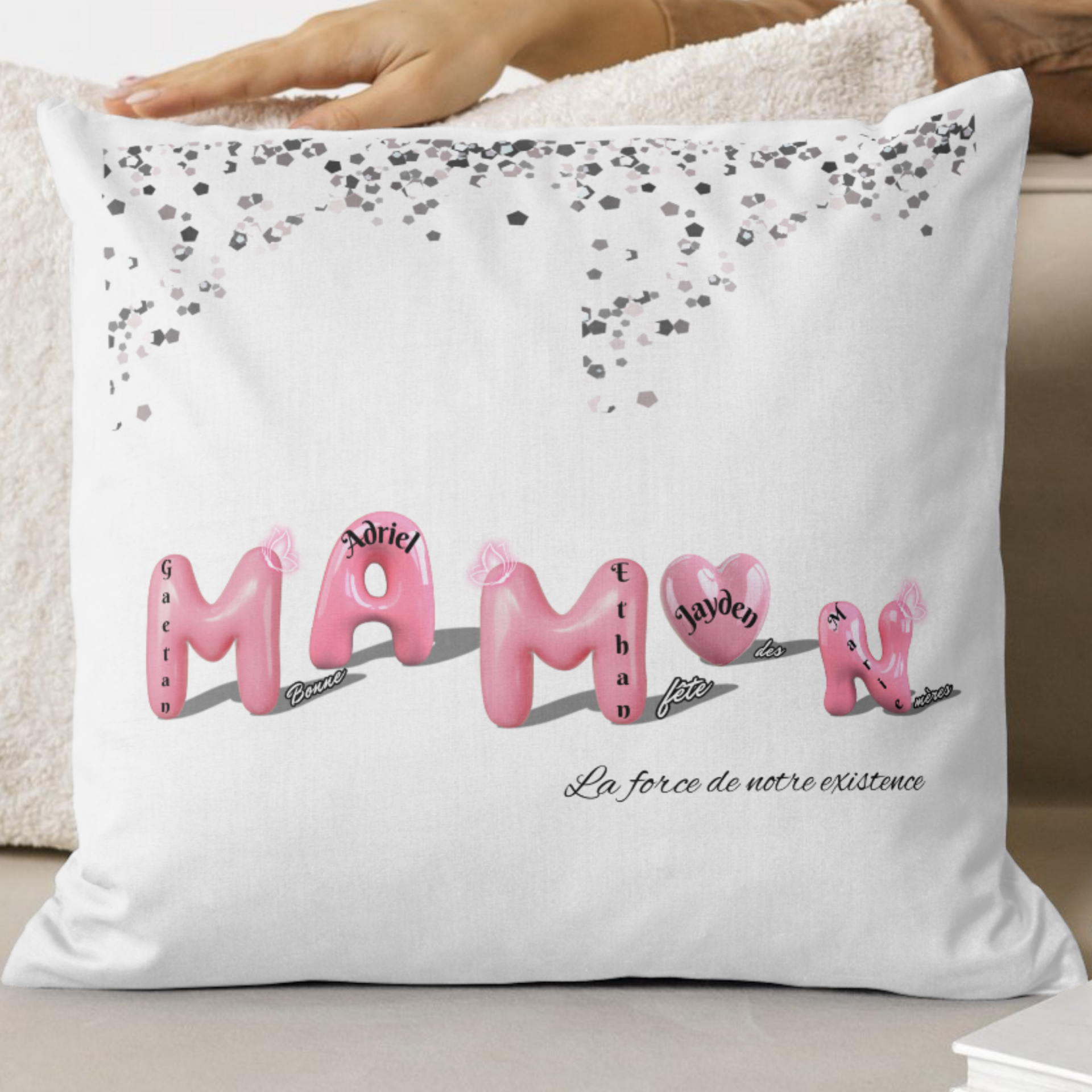 Housse de coussin personnalisée Fête des Mères avec lettres ballons roses formant “MAMAN”, prénoms des enfants intégrés dans chaque lettre, confettis argentés en haut et message au choix en bas.