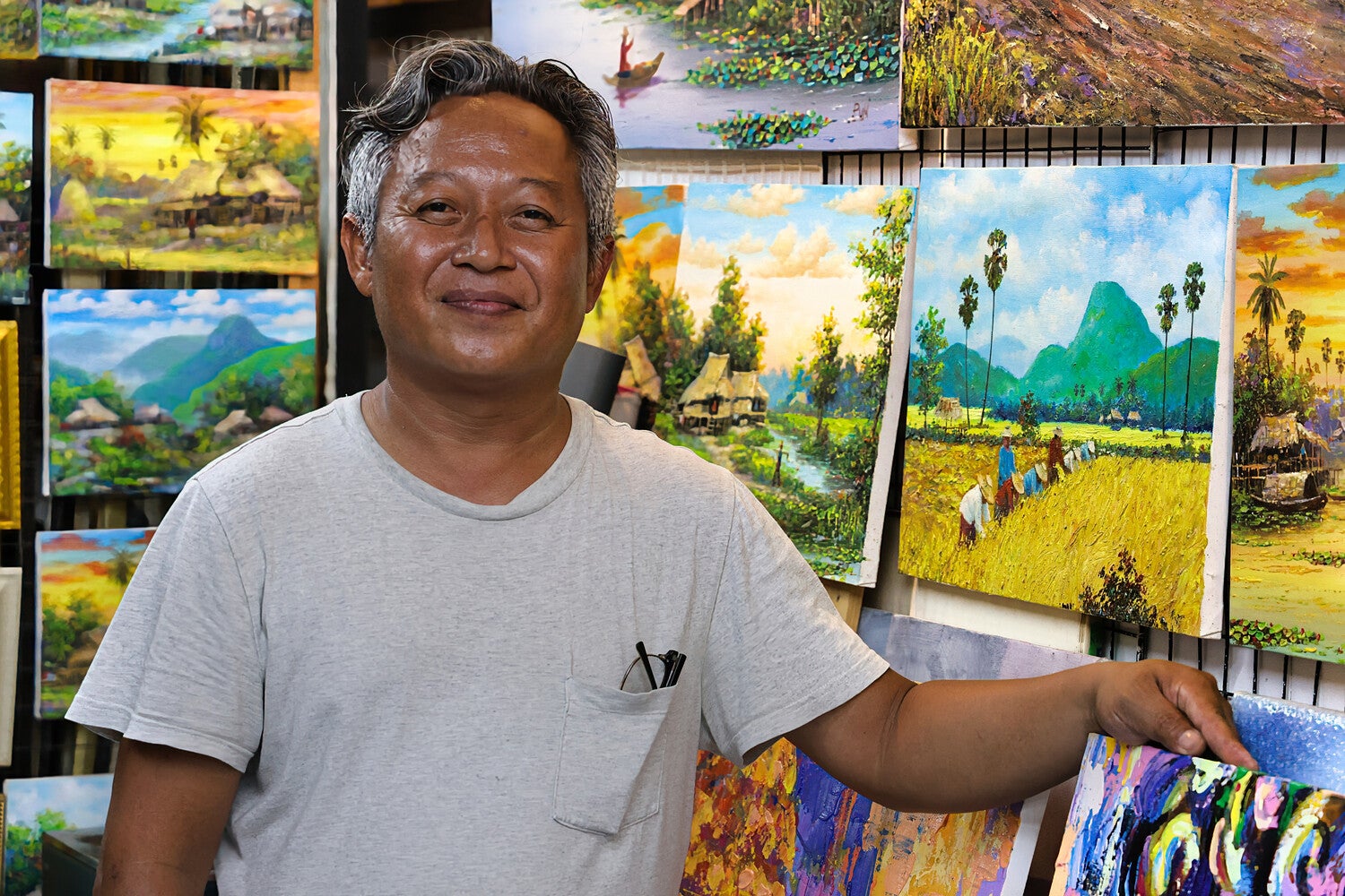 Kunstenaar Seksak Jaichumchen tussen schilderijen in atelier Thailand
