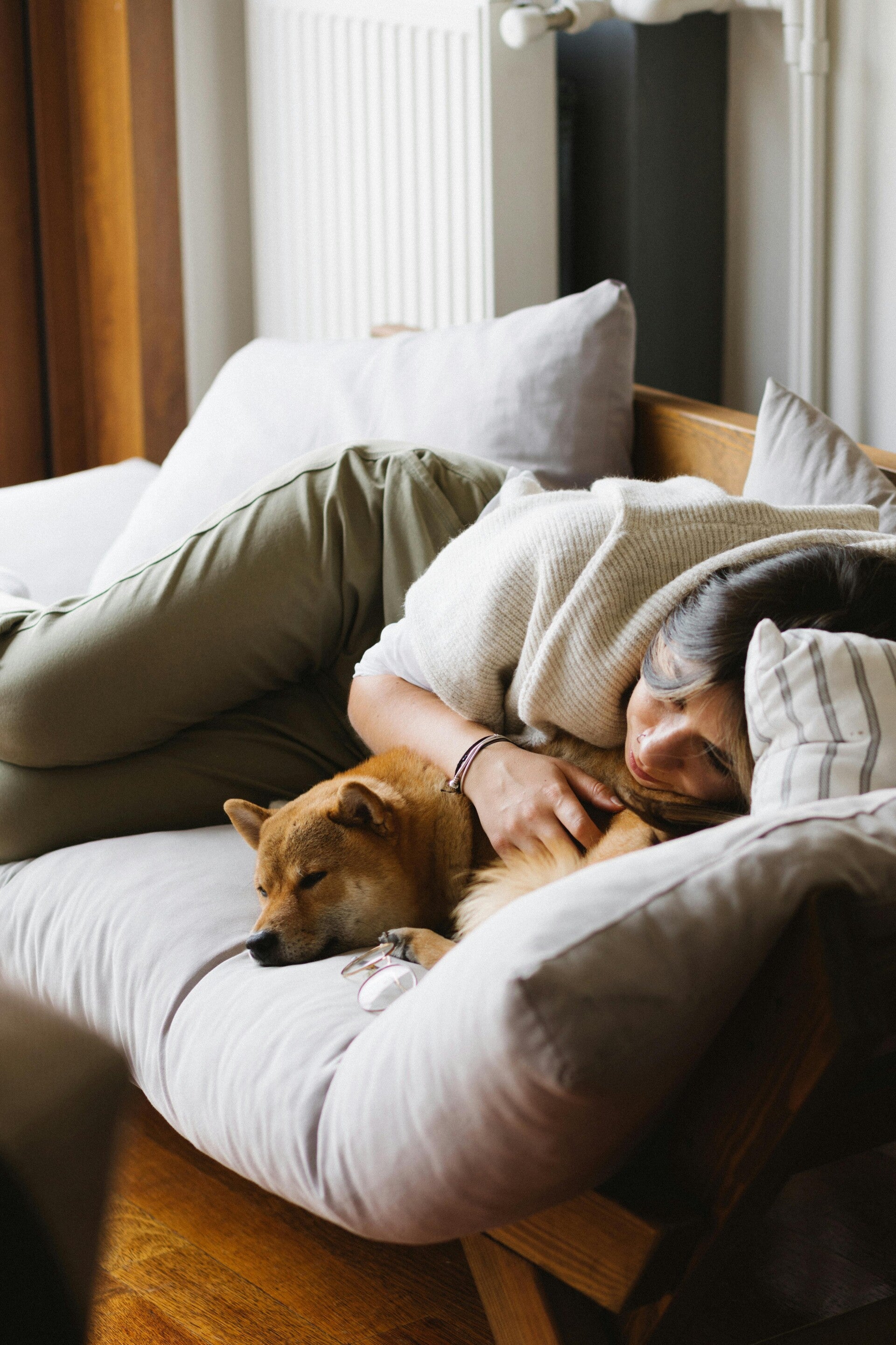 Ontspannen vrouw ligt op de bank met haar hond bij het raam, een moment van rust en zelfzorg tijdens de overgang.