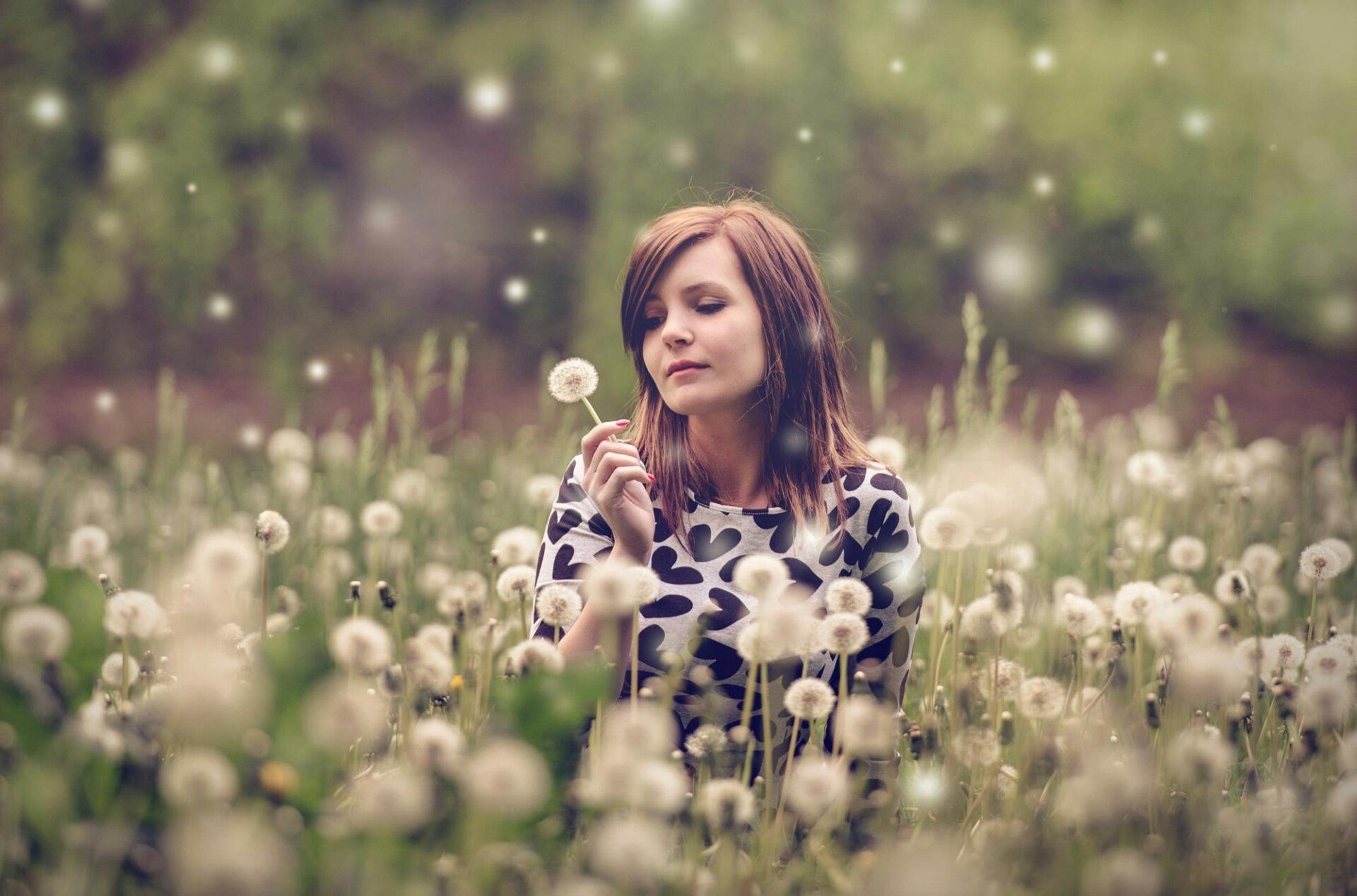 Vrouw staat in een veld en houdt een uitgebloeide paardenbloem vast — symbool voor loslaten en ontspanning in de lente.