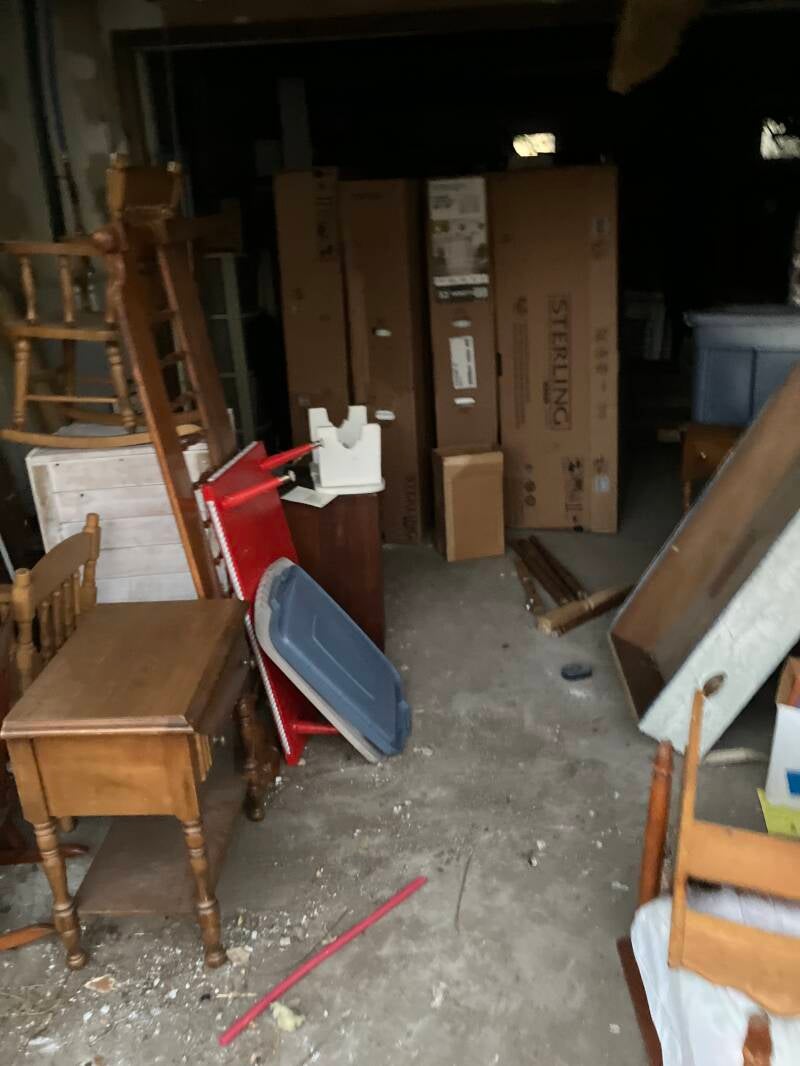 Storage area containing wooden chairs, boxes, and other household items.