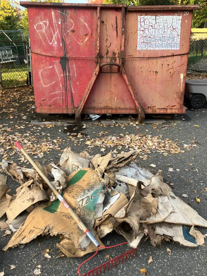 Outdoor debris and flattened cardboard gathered beside a dumpster.