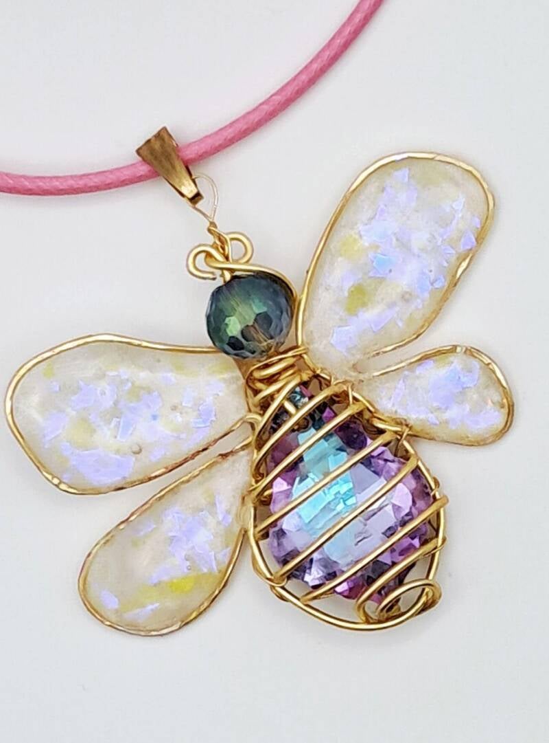 Hypoallergenic  gold-plated wire-wrapped bee pendant 5 X  5cm with opalescent resin wings and a crystal body on a pink cord. Price 40€