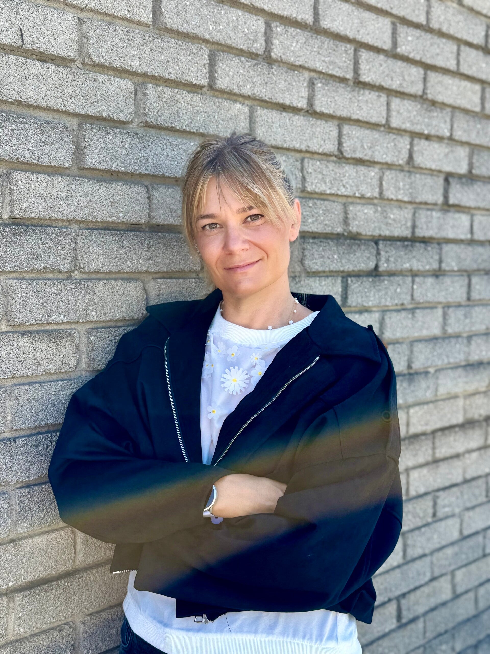 Jacqueline Pfanzelter in schwazer Jacke und weissem Tshirt vor grauer Ziegelwand