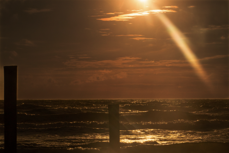 Zonlicht over de zee met houten paal – gouden uur aan de kust