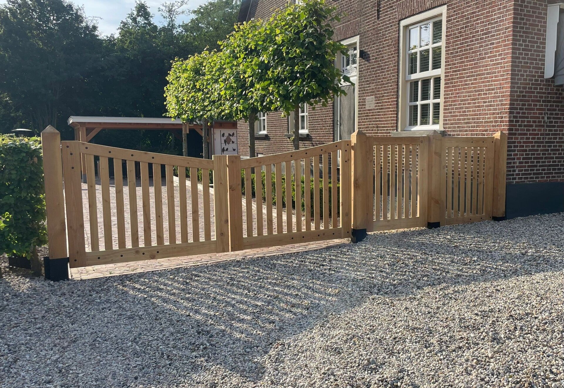 Houten toegangspoort in notarisstijl tussen twee antraciet kolommen met brievenbus.