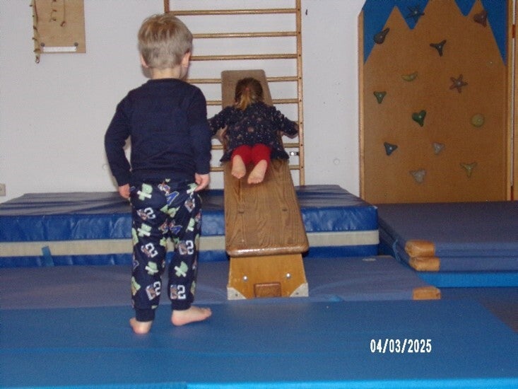 Kinder, die in der Turnhalle auf eine blaue Matte klettern