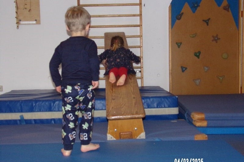 Kinder, die in der Turnhalle auf eine blaue Matte klettern