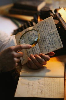 Historic handwritten papers being examined through a magnifying glass, representing the close study of UK war records and family military archives.