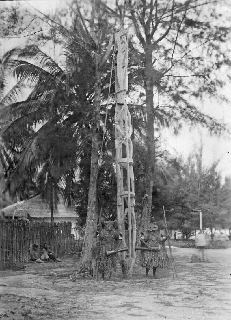 TM-60045621  Gemaskerde mannen bij een voorouderpaal tijdens een ritueel ter herdenking van overleden stamgenoten 1930-1940