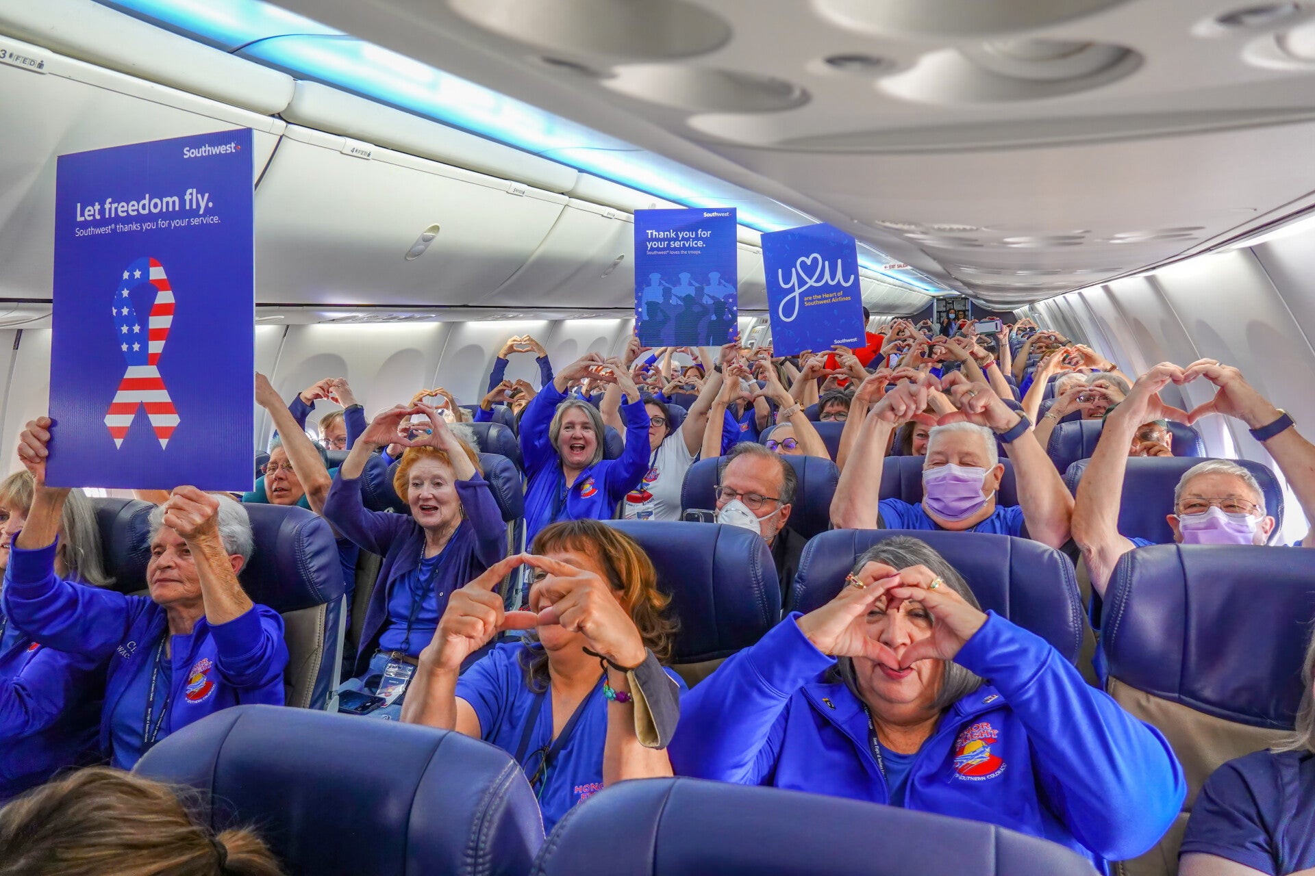 Veterans and volunteers on a Southwest Honor Flight making heart signs and holding thank‑you posters