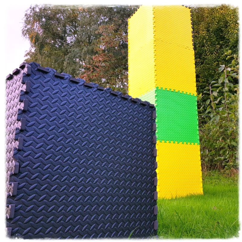 Een kubus van zwarte foam tegels op de voorgrond, met in de achtergrond een toren van 4 foam tegels hoog. Het hoort bij de GridGame Perspective, een serious game van Geck Genoeg.