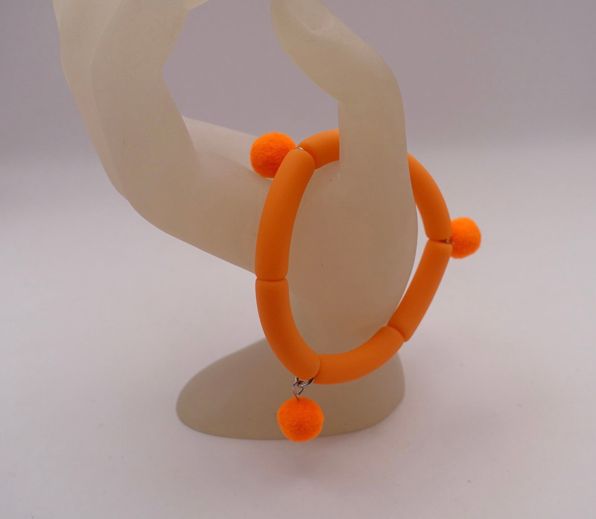 ARor010926: Mat oranje armbandje met pomponnetjes.