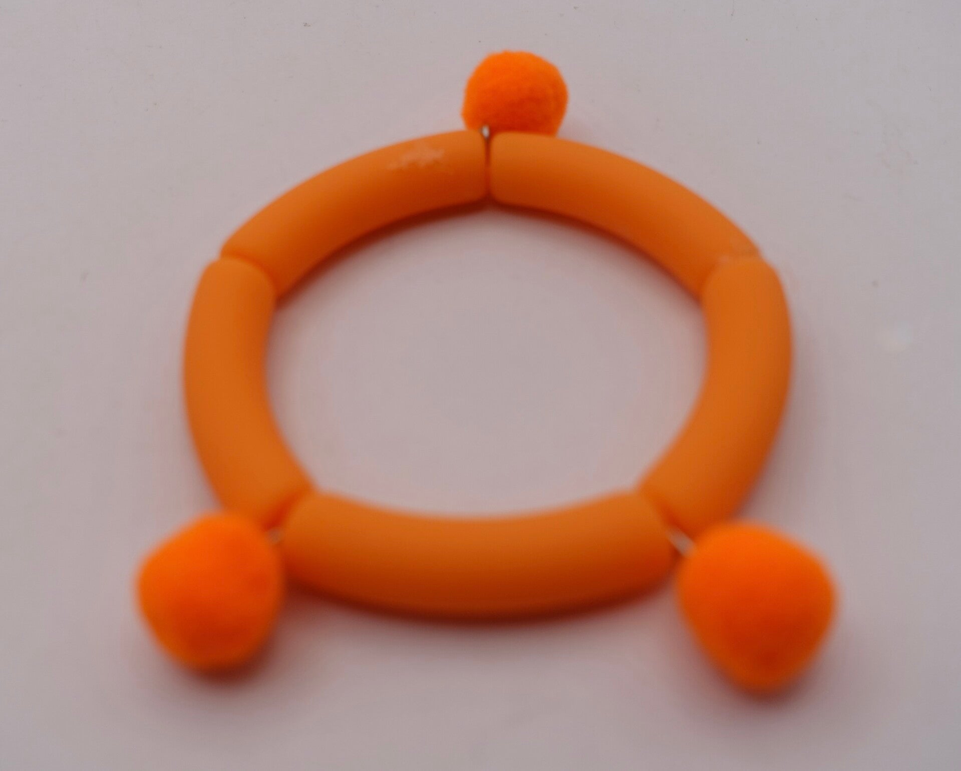 ARor020926: Mat oranje kinderarmbandje met pomponnetjes.