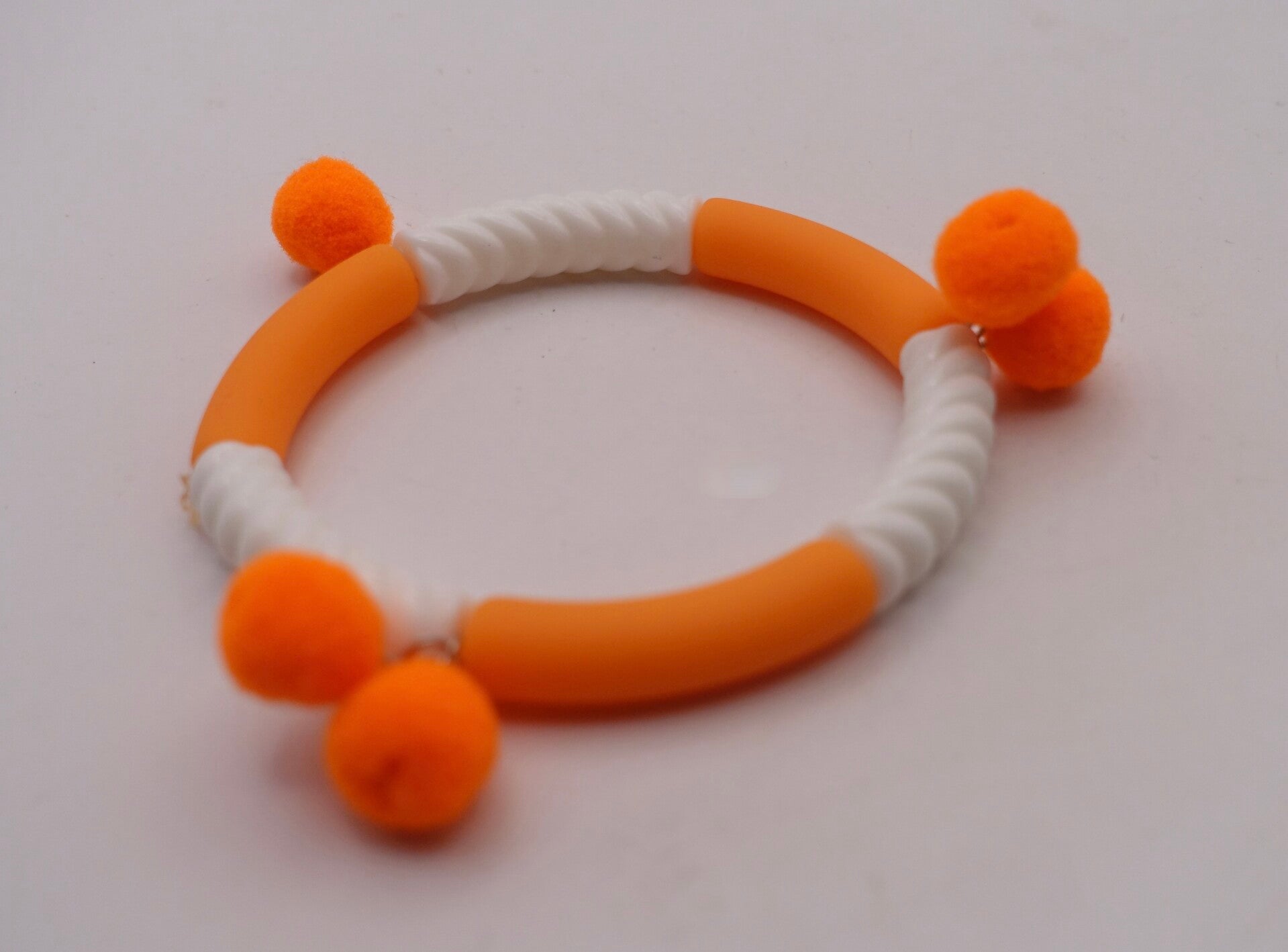 ARor030926: Mat oranje met wit geribbeld armbandje met pomponnetjes.