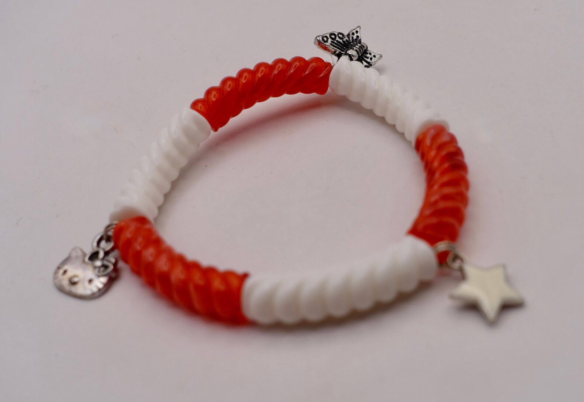 ARro010926: Rood met wit geribbeld armbandje met bedeltjes.