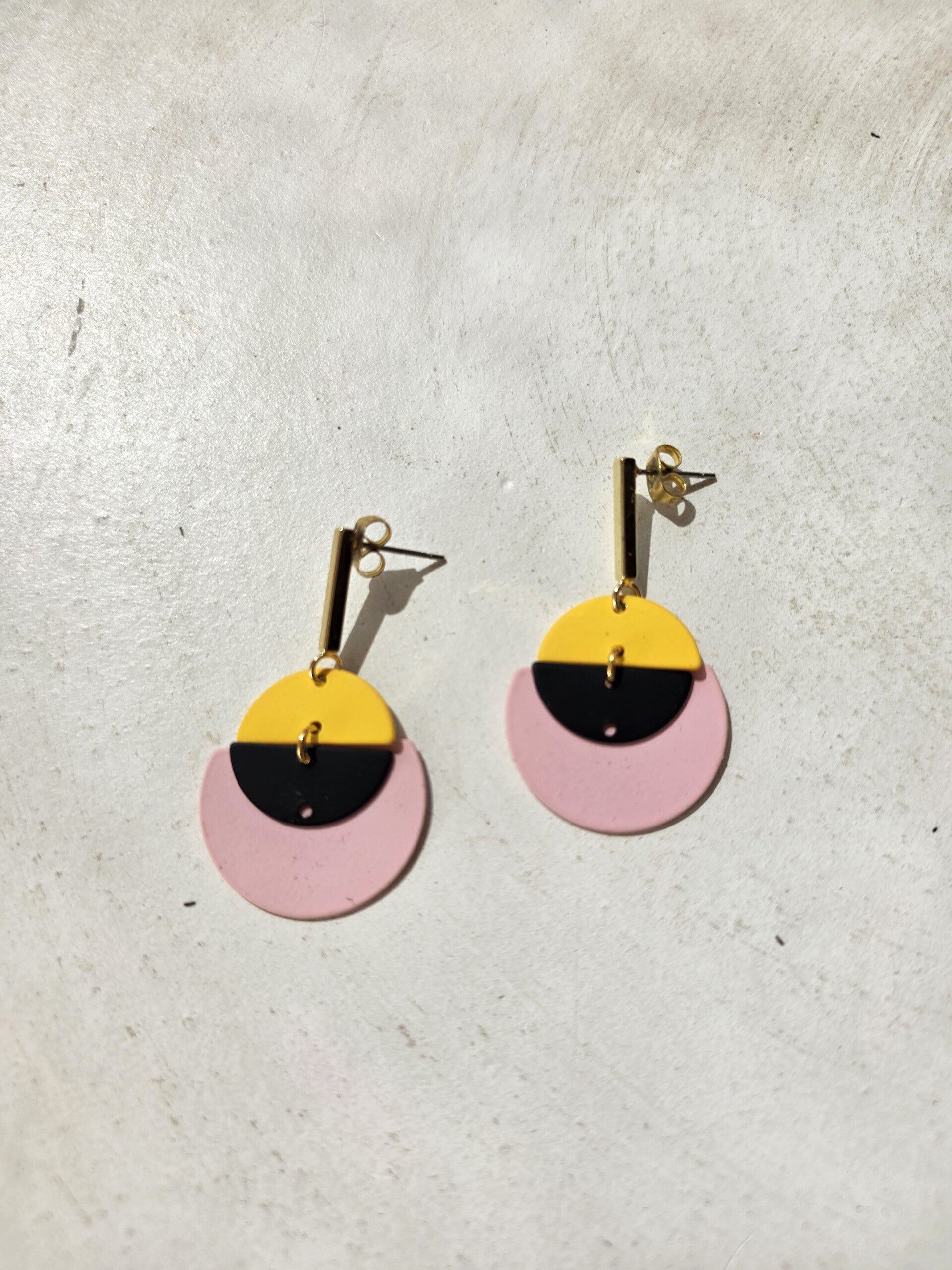 cirkelvormige oorbellen in geel, zwart en roze met rechthoekige oorstekers.