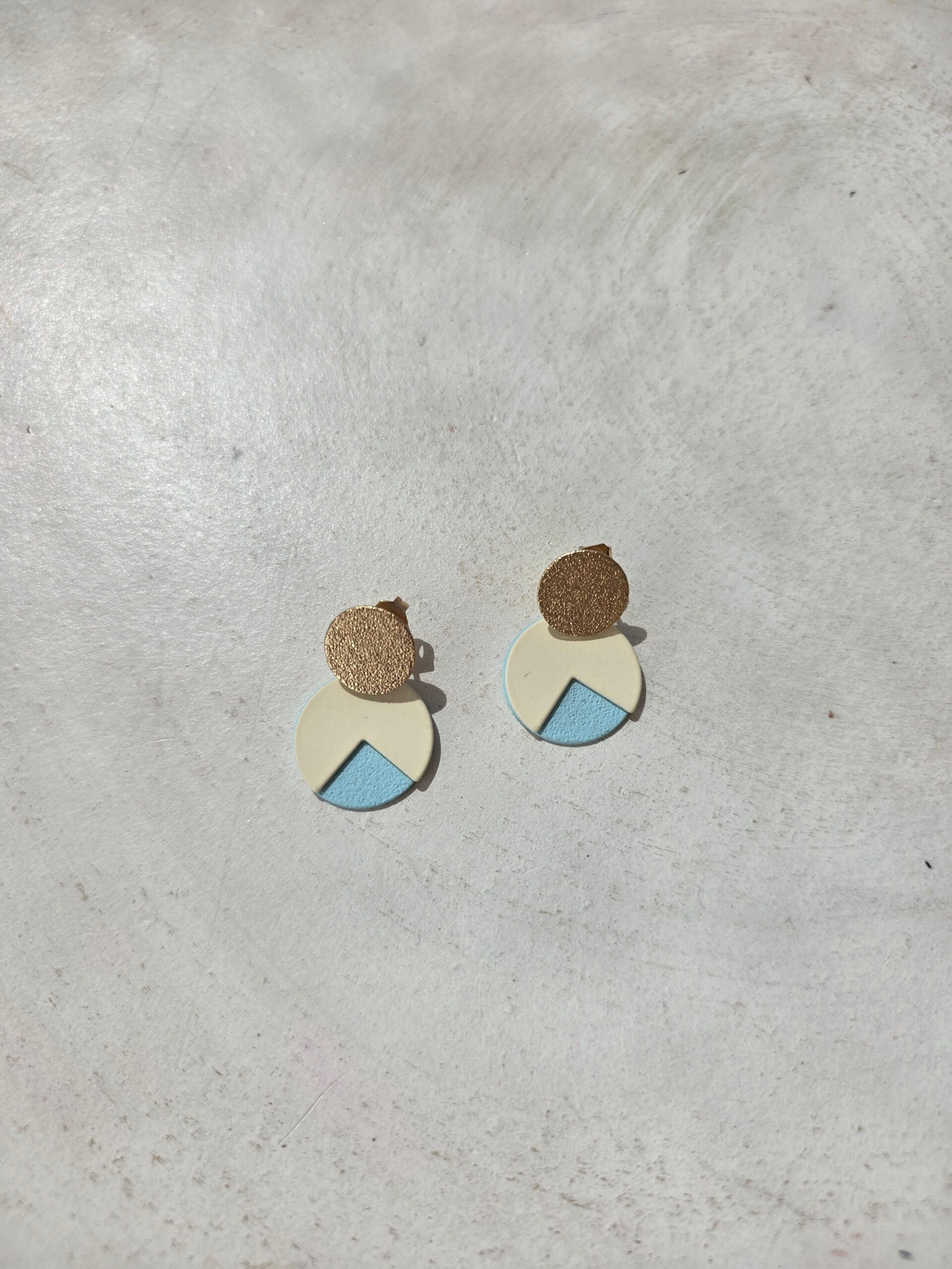 kleine cirkelvormige oorbellen in goud, wit en lichtblauw.