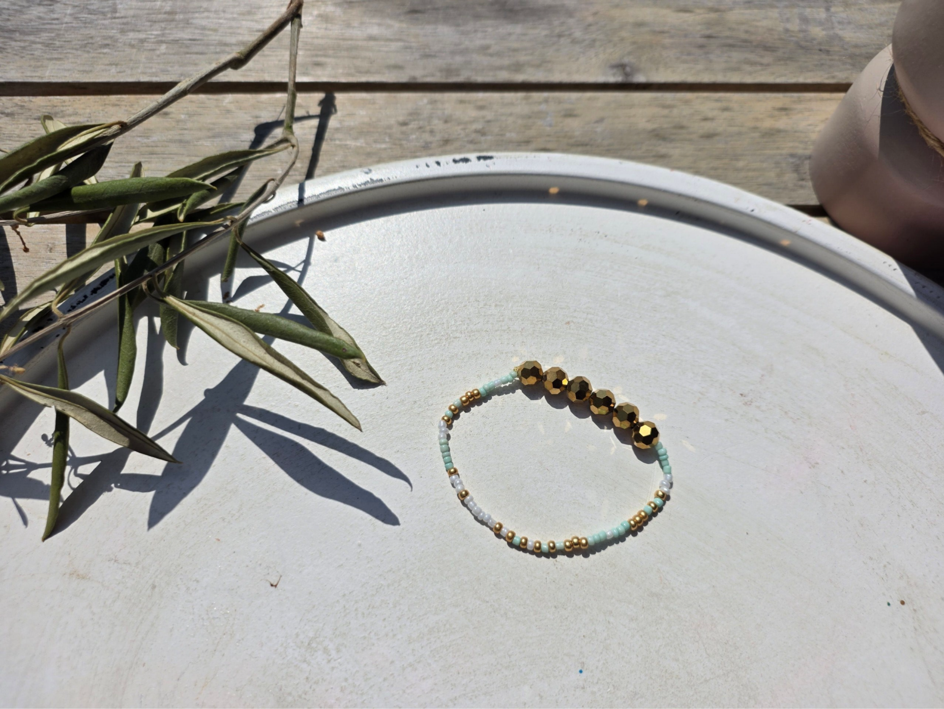armband uit rocailles (3mm) in wit, goud en mint afgewerkt met grote bronskleurige facetkralen