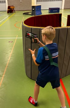 Kinderen spelen lasergame in een gymzaal in Ede, die is omgetoverd tot een game area, rennend, dekking zoekend en fanatiek spelend tijdens een actief en enthousiast kinderfeestje.