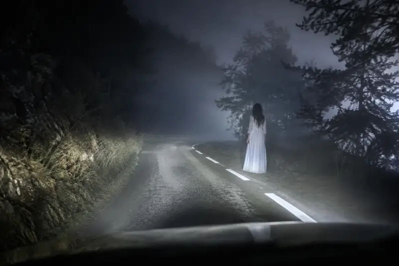 Illustration réaliste d'une Dame Blanche apparaissant au bord d'une route de nuit, inspirée des nombreux témoignages d'apparitions et de légendes paranormales.  Balise Title