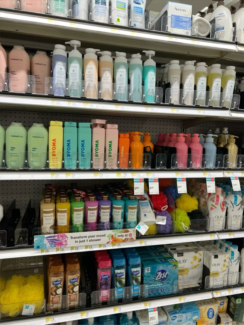 A retail aisle in a big-box store stacked with body washes, shampoos, lotions, soaps, and loofahs in pastel and bright colors. The polished consumer-facing end of the supply chain. The shelf the rabbit was tested for.