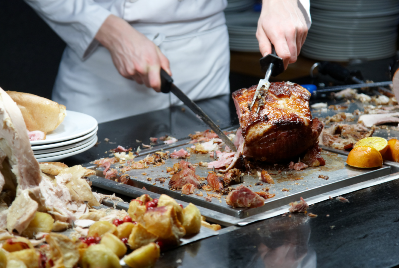 Chef carving roast beef at a carvery buffet with Yorkshire puddings and gravy