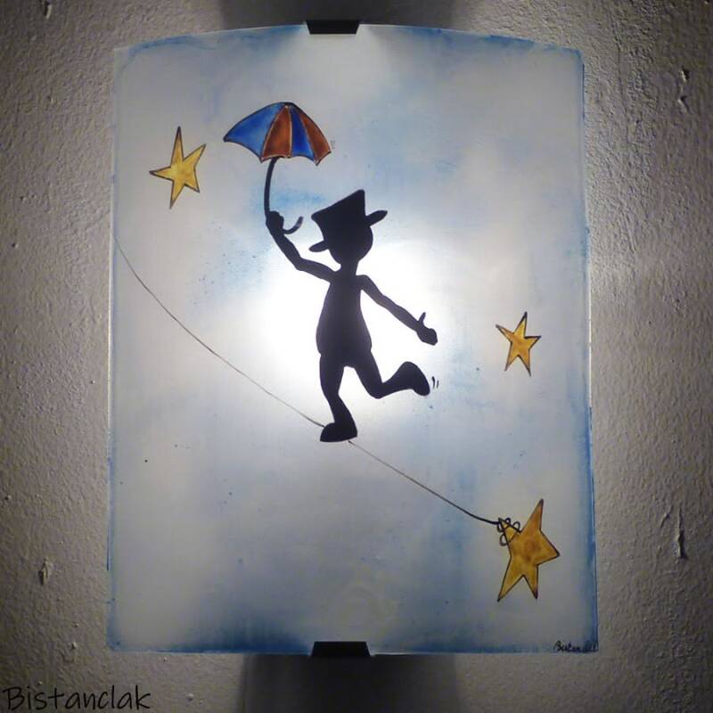 cettte applique murale bleutée au graphisme fantaisie est décorée d'un bonhomme avec un haut de forme et un parapluie en équilibre sur un fil tendu entre deux étoiles.