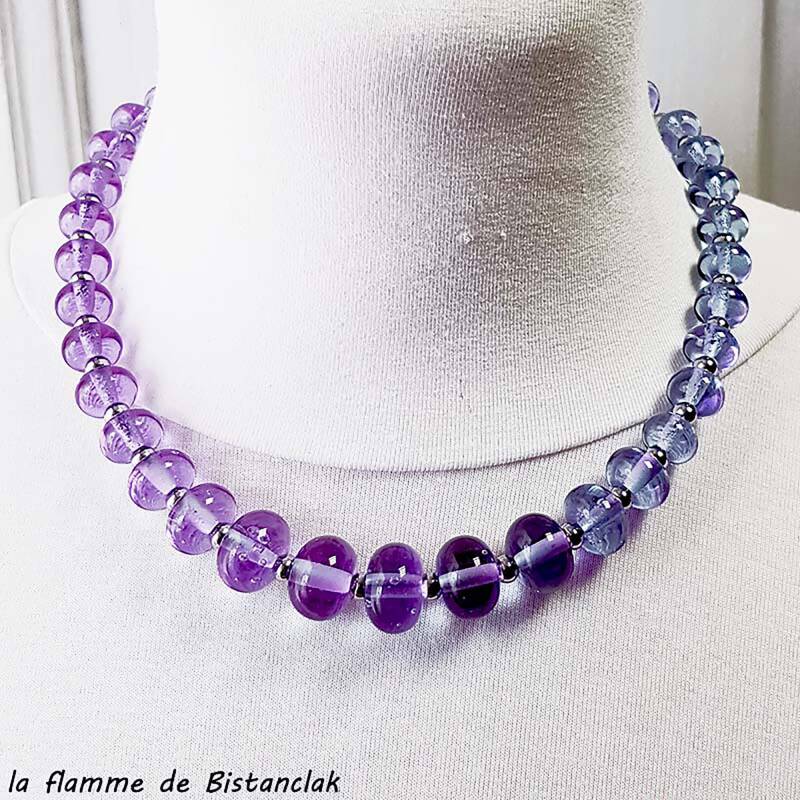 Un collier tout en perles de verre porté autour du cou, les perles rondes sont de couleur rose sur le côté gauche et sont bleues sur le côté droit, illustrant le verre alexandrite et ses changements de couleur selon l'exposition lumineuse.