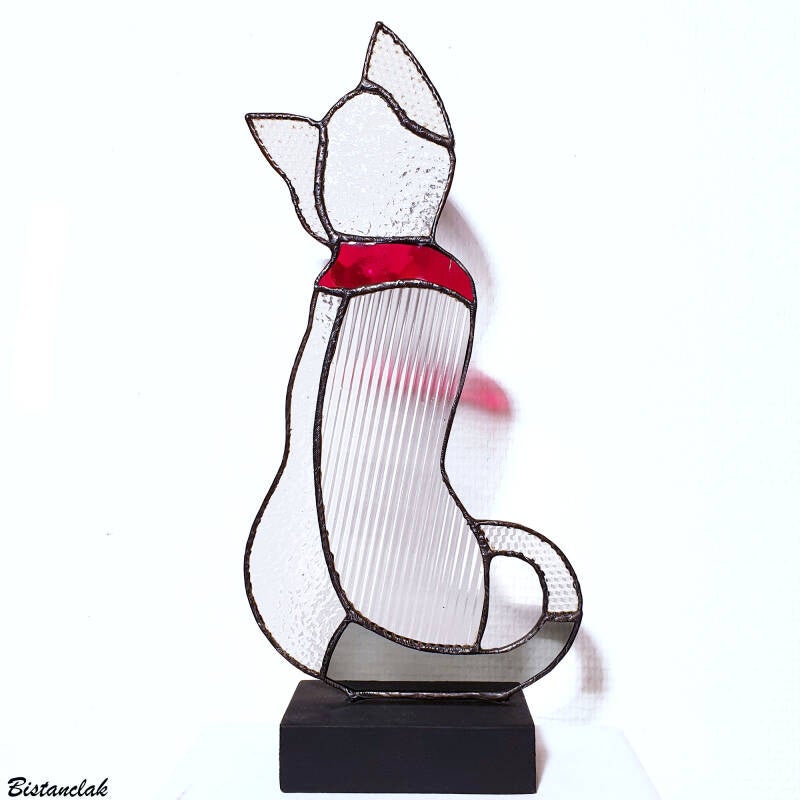 cet objet de décoration vitrail représente un chat, assis et de dos, en verre translucide incolore, rouge et gris.