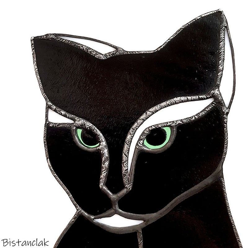 gros plan sur la tête du chat noir et blanc aux yeux verts orné des finitions constituant de petits motifs décoratifs sur les soudures.