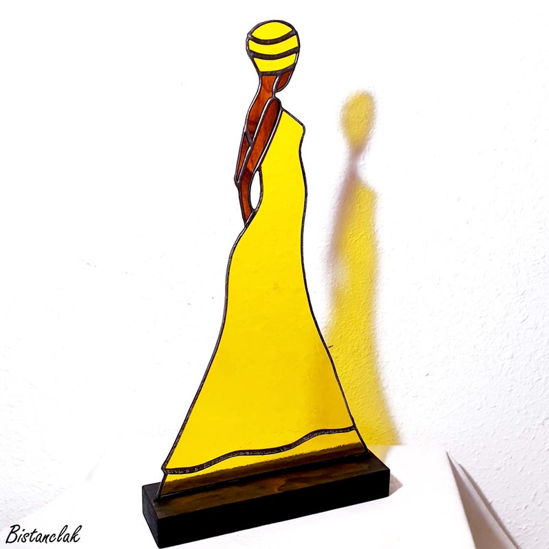 cette décoration vitrail représente une belle femme africaine élancée vêtue d'une longue robe jaune et coiffée d'un turban