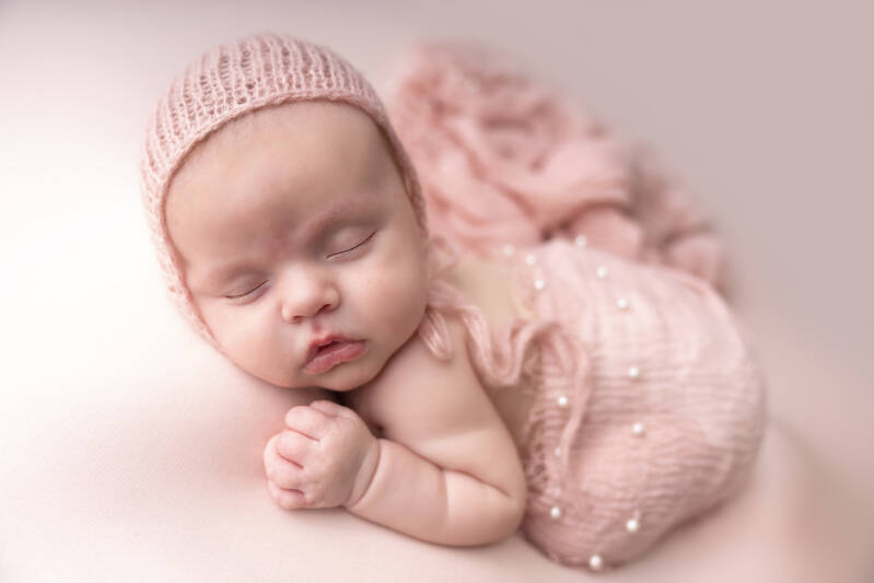 newborn baby girl sleeping with a pink hat on and a pink shawl cover